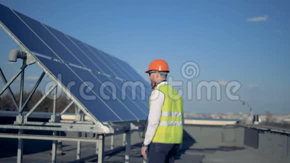 一个拿着笔记本电脑的男人对着相机微笑站在屋顶上的太阳能电池附近4K视频的预览图