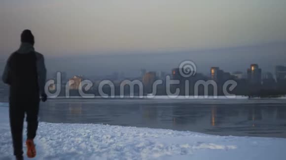 运动员跑步到冬季河岸与城市景观实现目标视频的预览图