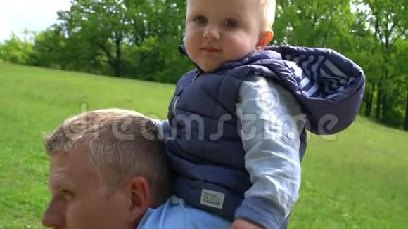 小男孩坐在他父亲的脖子上公园里梦见鸟的飞行父亲天视频的预览图