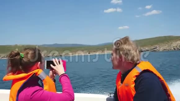 年轻夫妇穿着救生衣乘船游湖女孩用手机拍照3840x2160视频的预览图