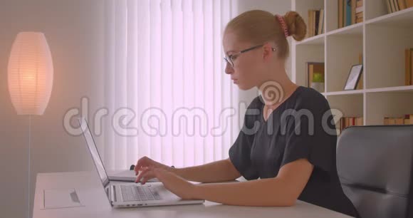 戴着眼镜手提电脑在办公室里看相机的年轻白种人女商人的特写照片视频的预览图