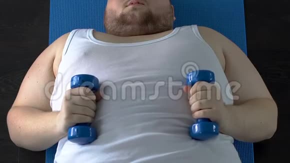虚弱的肌肉肥胖的男人举起哑铃努力躺在地板上健身视频的预览图
