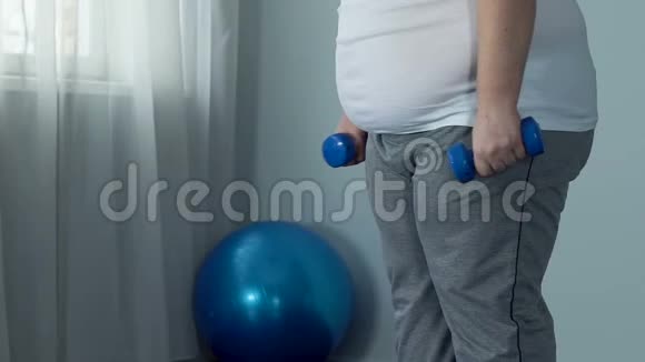 肥胖的单身汉手里拿着哑铃做蹲减肥锻炼计划视频的预览图