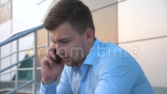 绝望的年轻商人在智能手机上交谈坐在办公楼附近的楼梯上关闭视频的预览图