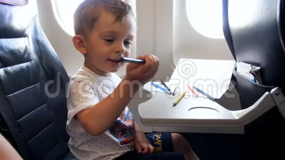 在飞机上长时间飞行时微笑的蹒跚学步的男孩画画的4k镜头视频的预览图