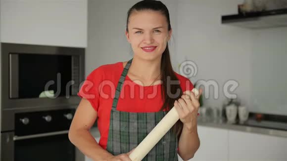 厨房背景中年轻微笑女孩的肖像她拿着滚针看上去很开心视频的预览图