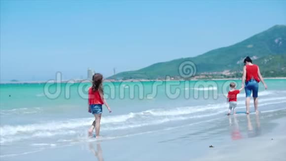 一个可爱的小女孩和她的母亲和弟弟沿着海滩散步看着飞机上的天空看着视频的预览图