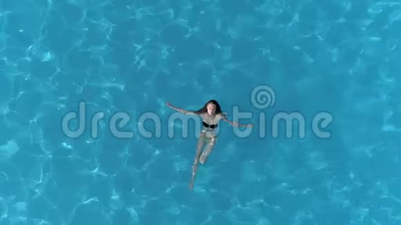 夏天穿泳装的游泳女孩在清澈的游泳池放松鸟瞰视频的预览图