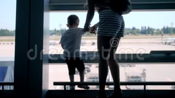 国际机场候机楼跑道上年轻母亲带着蹒跚学步的小男孩看飞机的4k视频视频的预览图