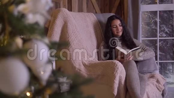 一个小女孩坐在圣诞树附近的椅子上看书视频的预览图