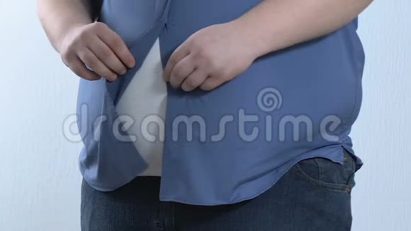 年轻的肥胖男性扣紧衬衫尝试超大布身体护理视频的预览图