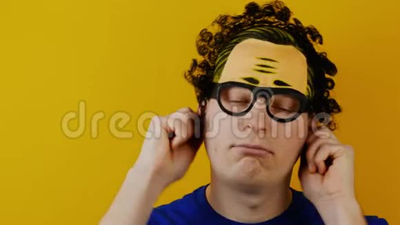 疯癫的卷发男子拉着自己的耳朵在黄色的墙上露出他的舌头欢快地笑着人类的情绪视频的预览图