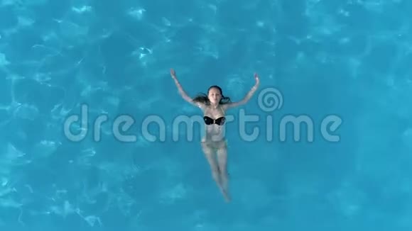 放松的女孩漂浮在清澈的游泳池里享受暑假鸟瞰视频的预览图