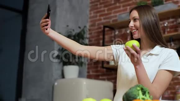 女人在家厨房用手机浏览年轻女子在智能手机上浏览微笑着快乐女人吃苹果视频的预览图
