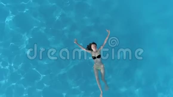 在假期里放松一下在清澈的游泳池里飞行无人机飞过比基尼女郎的上空视频的预览图