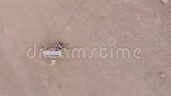 年轻的赤脚女人坐在沙漠里靠近一架白色的钢琴从上面看超真实的故事情节空中观景视频的预览图