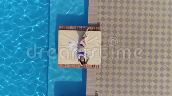 夏天飞过女孩的无人机躺在靠近游泳池的露台上上面有蓝色的美丽的水视频的预览图
