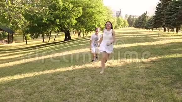 快乐的年轻夫妇在公园的草地上奔跑慢动作视频的预览图