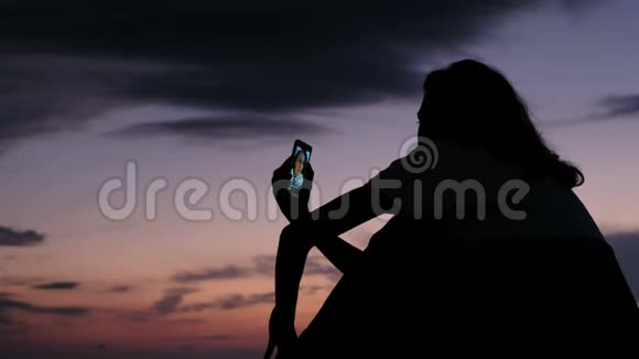 日落时分一个女孩用智能手机在社交网络上生活视频的预览图