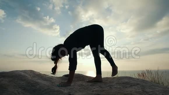 在日出时在石头上做杂技瑜伽的瘦女人视频的预览图