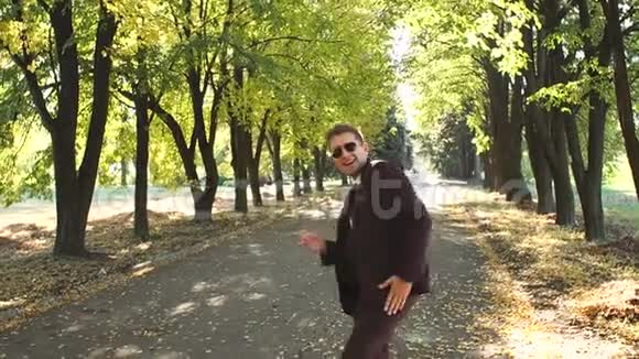 一个穿西装戴太阳镜在秋天公园跳舞的成功商人视频的预览图