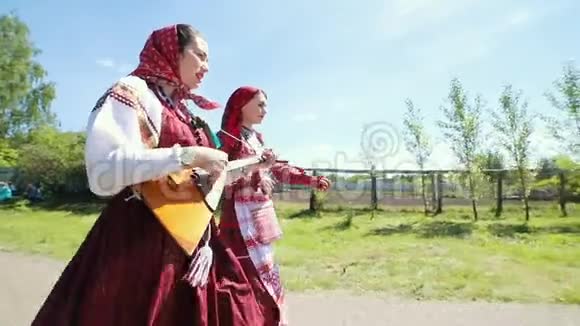 两个穿着俄罗斯传统服装的年轻妇女在村里的道路上行走视频的预览图