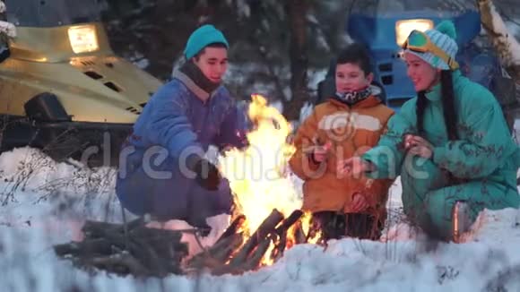 冬季森林一家人坐在火边的树林里聊天炸香肠视频的预览图