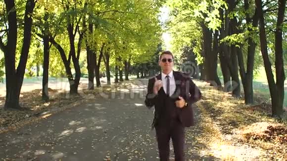 一个穿西装戴太阳镜在秋天公园跳舞的成功商人视频的预览图