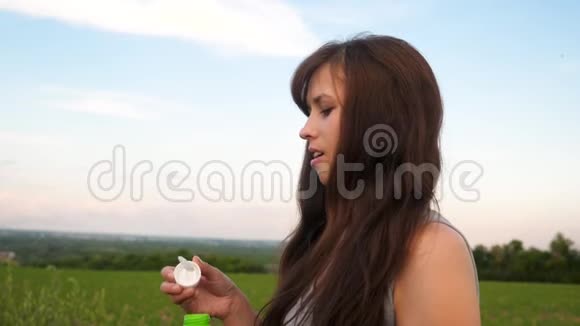 美丽的女孩长发吹着透明的肥皂泡在蓝天和微笑慢动作视频的预览图