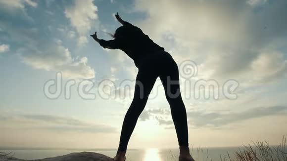 日出时女性的剪影在悬崖上升温视频的预览图