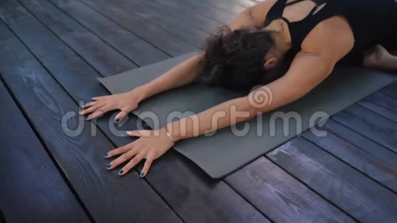 穿着运动服的年轻女子独自在木制甲板上练习瑜伽女孩躺在健身垫上做身体伸展运动视频的预览图