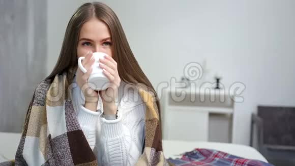 年轻迷人的女人裹着温暖的格子拿着杯子喝热饮料的肖像视频的预览图