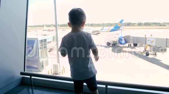 后视4k镜头小男孩站在机场候机楼透过大窗户看喷气式飞机视频的预览图