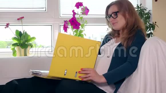沮丧的孕妇拇指夹和文件坐在家里的沙发上视频的预览图