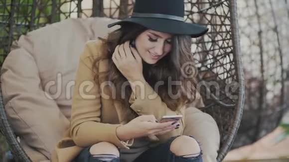 迷人可爱的女孩可爱的微笑摆动在秋千上特写慢动作他手里拿着智能手机视频的预览图