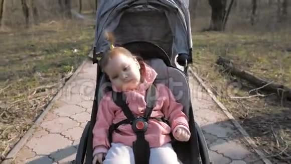 年轻的母亲和一个小女孩在公园的婴儿车里散步视频的预览图