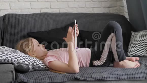 十几岁的女孩玩平板电脑躺在家里的沙发上人技术和休闲理念视频的预览图