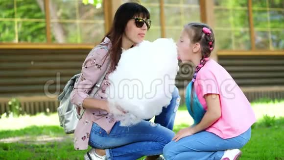 布鲁内特女士戴着太阳镜带着她的女儿8岁的女孩扎着蓝色的辫子吃着香甜的棉花视频的预览图