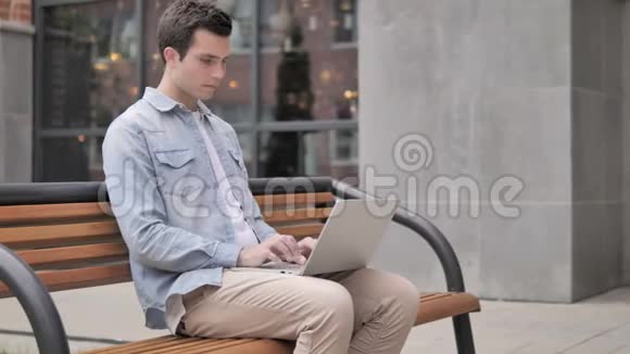 脖子疼的年轻人在户外使用笔记本电脑视频的预览图