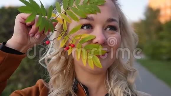 一个美丽的年轻金发女郎的肖像脸附近有一堆山灰秋天在一个城市公园里拍摄慢动作视频的预览图