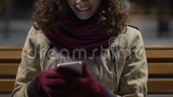 迷人的快乐的混血女孩带着手套使用智能手机视频的预览图