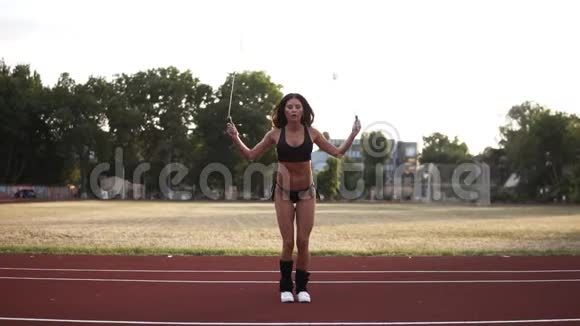 健身慢动作穿黑色比基尼的女士跳跃在户外体育场使用跳绳正面观点视频的预览图