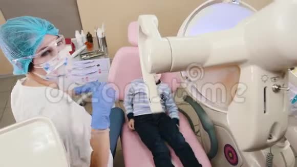 牙科医生的一个小男孩坐在病人的椅子上牙医打开灯张开嘴视频的预览图