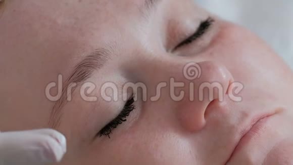 一位戴着白手套的专业美容师的双手在一位美女的眼睛周围涂抹眼霜视频的预览图