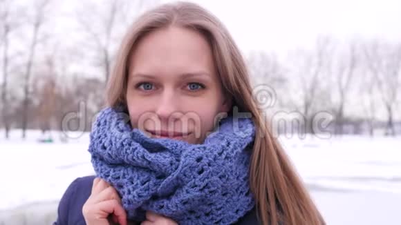 穿着蓝色针织围巾的漂亮蓝眼睛女人在冬天的城市公园里她看着摄像机纠正着她的长尾巴视频的预览图