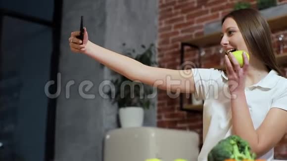 女人在家厨房用手机浏览年轻女子在智能手机上浏览微笑着快乐女人吃苹果视频的预览图