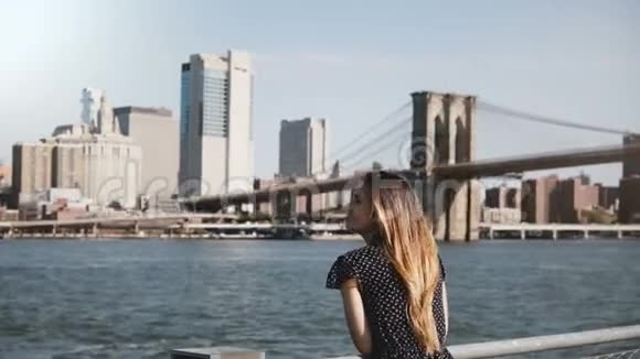 迷人的景色快乐的微笑的欧洲妇女与飞扬的头发享受著名的纽约天际线和布鲁克林大桥的景色视频的预览图