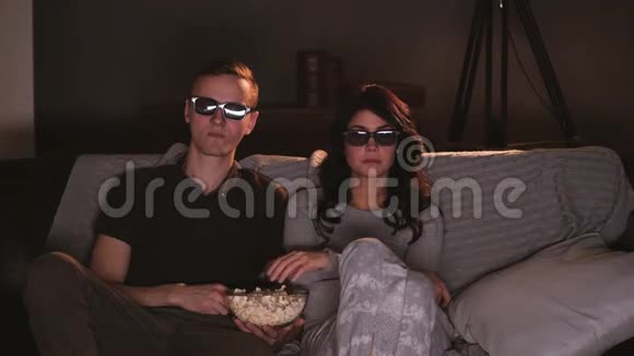 年轻夫妇在家用3D眼镜看电视吃爆米花视频的预览图