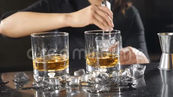 女酒保慢慢地把冰块和威士忌放进杯子里冰飞溅而下年轻女子视频的预览图