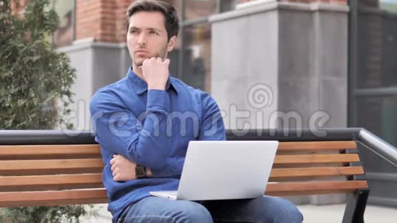 在笔记本电脑上工作的进攻性年轻人坐在室外的长凳上视频的预览图